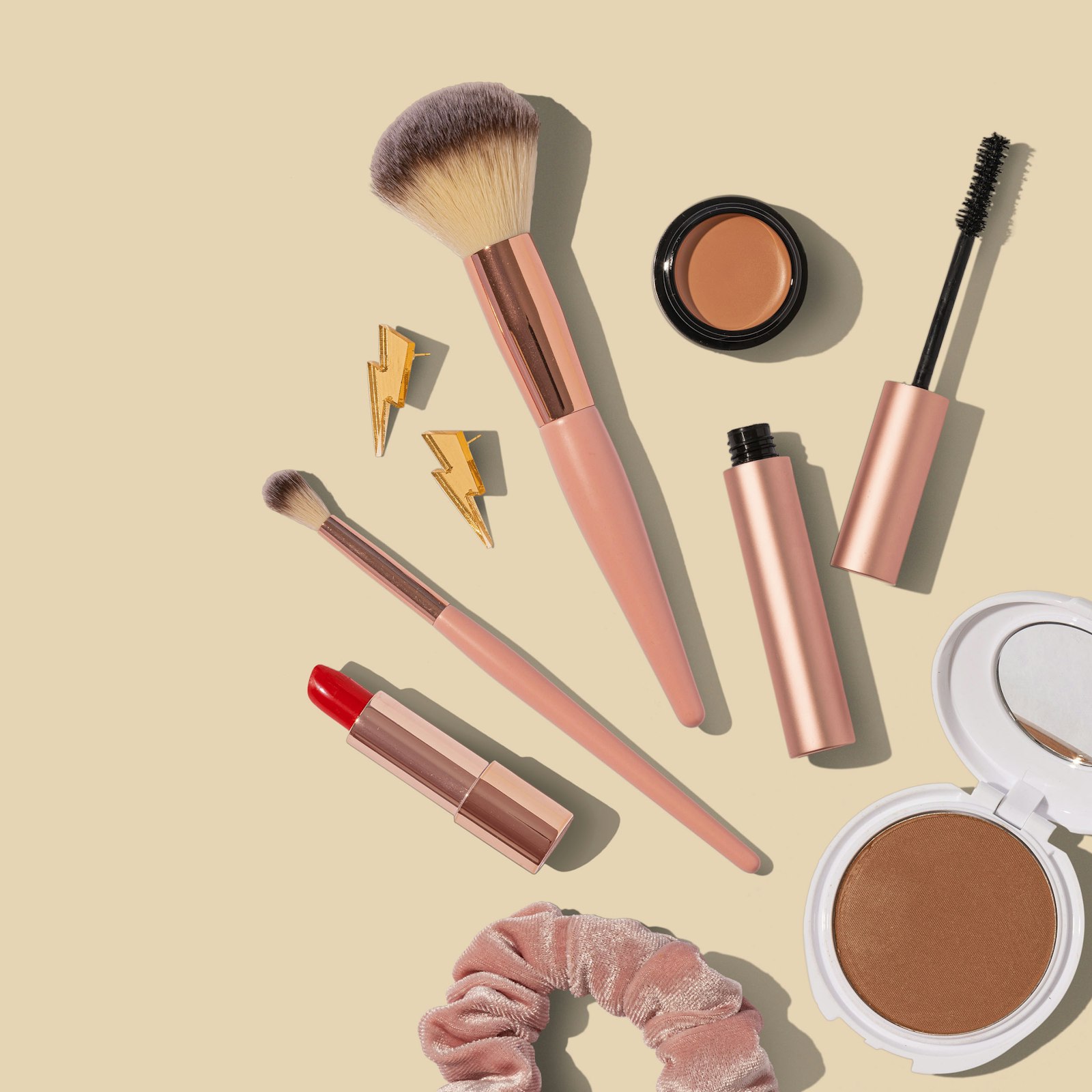 A row of beauty products lined on a marble vanity: foundation, primer, setting spray, mascara, and a single tube of lipstick.